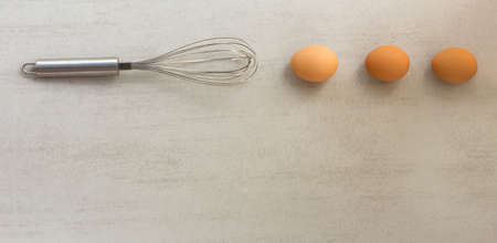 Steel whisk and eggs lined in a row on grey background. with space for textの写真素材