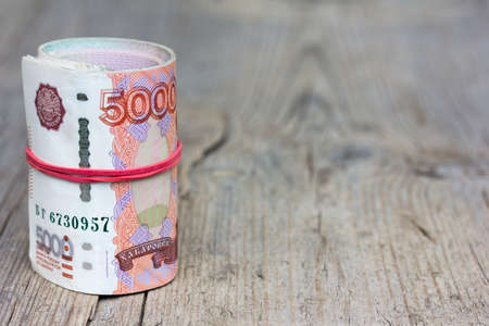 Roll Russian banknotes on old gray wooden board with cracks. Selective focus. with space for text placementの写真素材