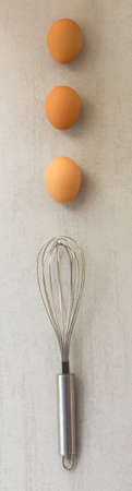 eggs are laid in a row and steel whisk on a gray backgroundの写真素材