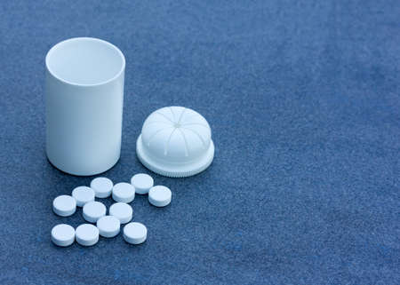White Pills scattered across a Blue Background and an Open Bottle. Top View Closeup. With Space For Your Textの写真素材