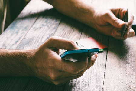 Man Hands holding credit card and using mobile phone in the evening. Online shopping, online banking and online marketing. shallow depth of field, toning photoの写真素材