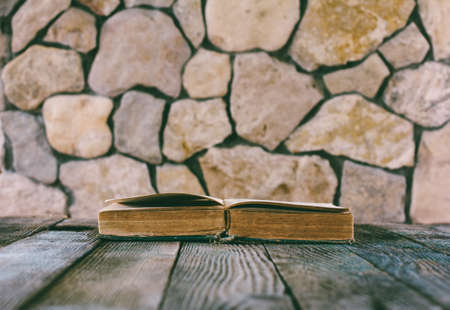 open old book on old wooden table on a background of stone walls. selective focus, toning photo. with space for your textの写真素材