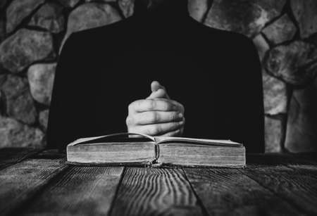 male in black clothes in front of an old open book. the concept of prayer, study, witchcraft. selective focus, black & white photoの写真素材
