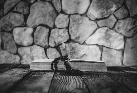prayer beads with a cross on an open old book on old wooden table on a background of stone walls. selective focus, black & white photo. with space for your textの写真素材