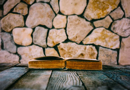 old open book on old wooden table on a background of stone walls. selective focus, toning photo. with space for your textの写真素材
