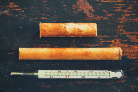 old medical mercury thermometer and a paper box on a black grunge wooden background close up, top...