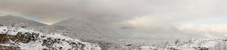 panorama landscape of wooded hills in the snow and the clouds and the mountain village in the...