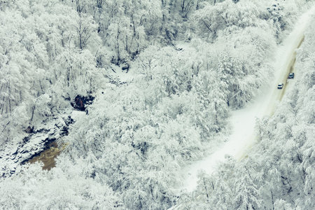 cars driving on winter snowy forest road along the river, the view from the top