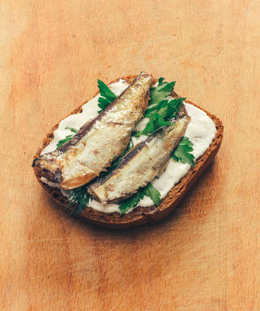 sandwich of canned sprats on rye bread with mayonnaise and parsley, and dill on a wooden cutting board close upの写真素材