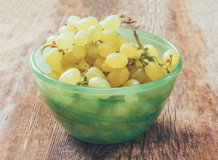 white grapes in a green bowl on old rustic wooden Board cracked. close up, tinted photoの写真素材