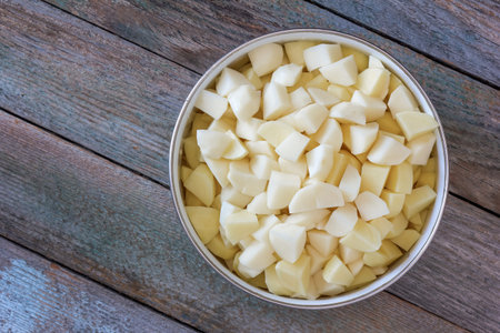sliced pieces of raw potatoes in a circular bowl on an old rustic wooden table. top view closeupの写真素材