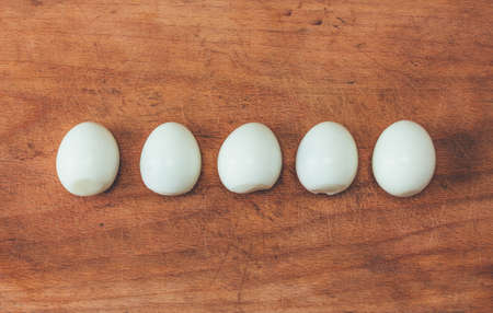 five cooked peeled eggs in a row on an old cutting board. view from above close-up, toning photoの写真素材