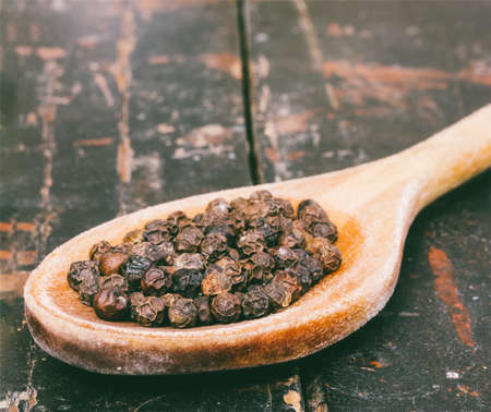 black pepper in wooden spoon on old rustic table closeupの写真素材