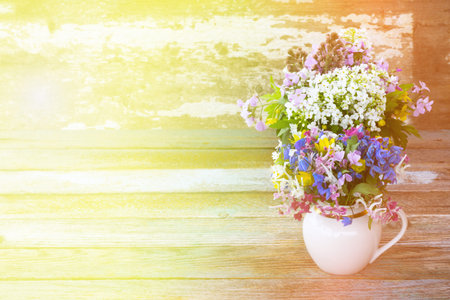 spring background with wild flowers in a white jug in bright sunlightの写真素材