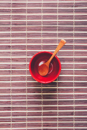Wooden spoon in an empty red cup on a brown bamboo mat, selective focus. Flat lay, top viewの写真素材