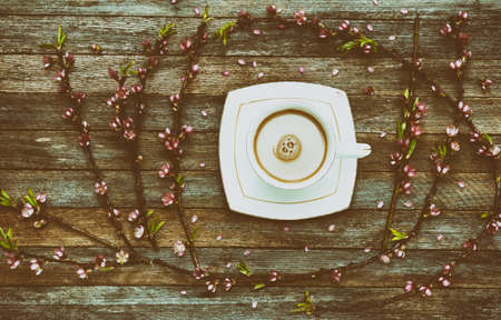 Cup of coffee milk and a frame of peach branches with pink flowers on wooden background from barn boards, top view. retro tinted photoの写真素材
