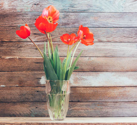 Bouquet of flowers of red tulips in a glass vase on a background of wooden granary boards close-upの写真素材