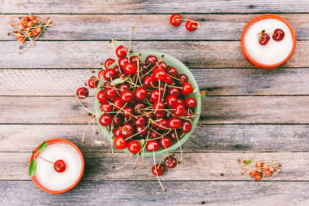 Green bowl with ripe cherry berries and cups with sugar on a wooden background, top view toned photoの写真素材