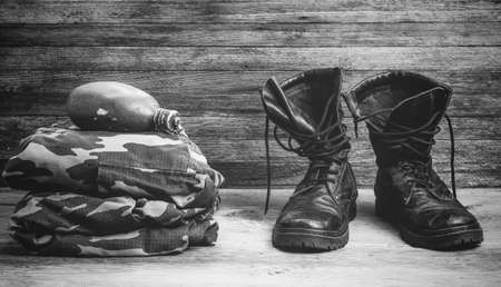 old leather black mens boots, military uniform and flask for water on a wooden background front view close-up, black and white photoの写真素材