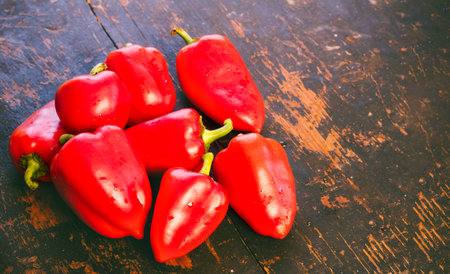 bunch of fresh ripe red bell peppers on an old black wood grunge background with space for text