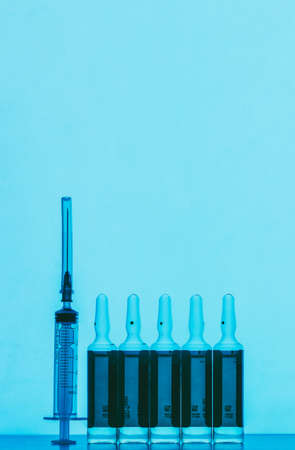 a disposable syringe and ampoules with a solution for injection on a blue background with space for textの写真素材