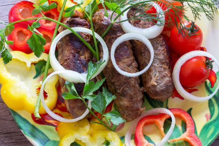 lula kebab of pork and beef on a plate with chopped onion, bell pepper and sprigs of dill, parsley and tomatoes closeupの写真素材