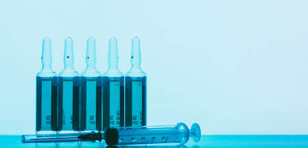ampoules with a solution for injection and a disposable syringe on a blue background with space for textの写真素材