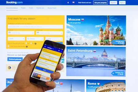 Adygea, Russia - January 16, 2018: The home page of the Internet booking of hotels booking.com on the screen the Chinese Xiaomi smartphone in male hand on a computer monitorのeditorial素材