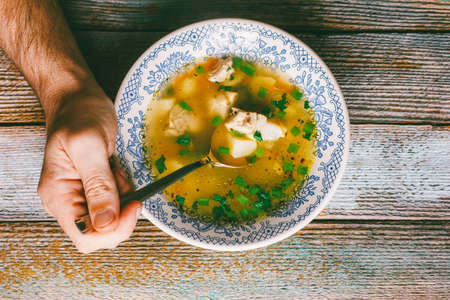 man eating diet chicken soup with green parsley on a wooden table close-up top viewの写真素材