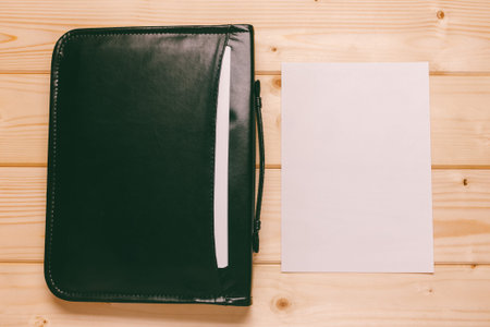 black leather briefcase with papers and blank white sheet of paper, close-up top view. mock up for...