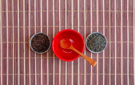 leaves of green tea and black tea in small saucers and an empty red violet with a wooden spoon on a...