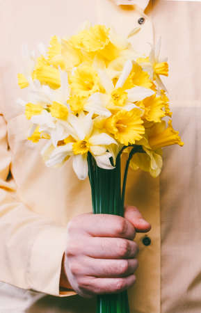 a man in a yellow shirt holding a bouquet of daffodils flowersの写真素材