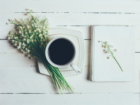 Book, Cup of coffee and bouquet of Lily of the valley flowers on white wooden table, top view