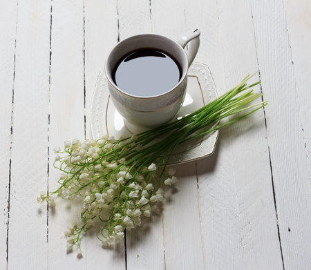 coffee Cup and bouquet of Lily of the valley flowers on white wooden table, top view