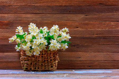 bouquet of Jasmine flowers in a woven straw basket on a table on a brown wooden retro background with copy spaceの写真素材