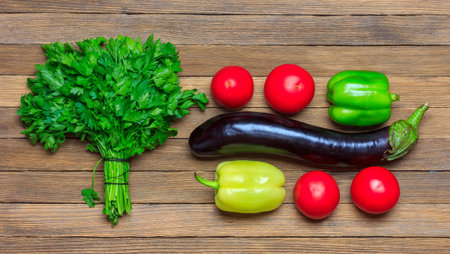 a set of vegetables aubergine, tomatoes, a bunch of parsley and a bell pepper on a wooden...