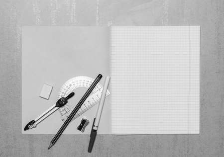 open school notebook mock up with copy space, ballpoint pen, pencil, eraser, compasses, steel protractor and pencil sharpener top view, black and white photoの写真素材