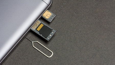 mobile phone and open slots for nano SIM cards, micro SD drive and metal key on grey background with...