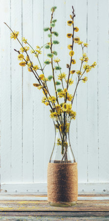 bouquet of flowering branches of willow and dogwood in a vase on the table on a white wooden...