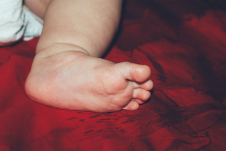 leg of a sleeping four month old baby on a red bed