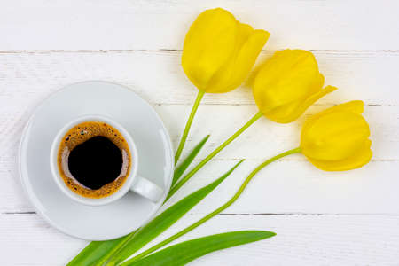 a Cup of black coffee on a saucer and a three yellow Tulip flower on a white wooden background closeup, top view flat layの写真素材
