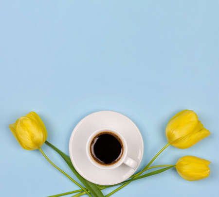 a Cup of black coffee on a saucer and a yellow Tulip flower on a blue background with copy space, close-up top view flat layの写真素材