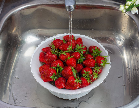 berries of ripe sweet strawberries in a white Cup of water in the sink under the pressure of tap...