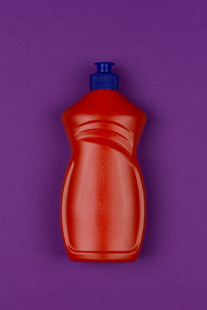 orange plastic bottle of dishwashing liquid on purple background close-up top view