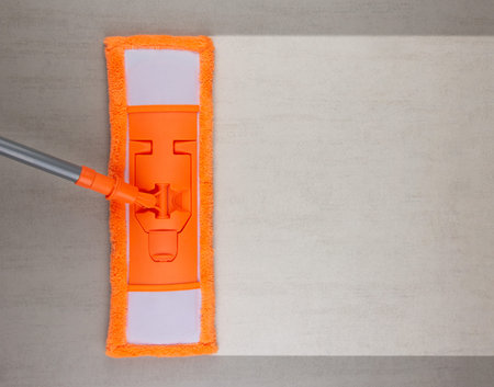 Cleaning grey ceramic floor with orange mop, top view with copy space