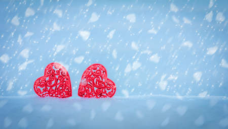 Valentine's Day Valentine card with two red openwork hearts in a snowdrift on a blue background with falling snowflakes in the shape of hearts with copy spaceの写真素材