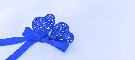 background for Valentine greeting card for Valentine's day, Christmas or new year two hearts classic blue color tied with blue ribbon on snow with copy spaceの写真素材
