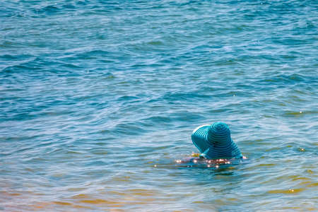 a woman in a big blue hat swims in the sea on a summer dayの写真素材