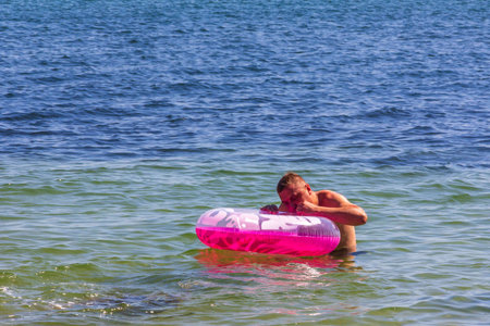 Kerch, Russia - 12 August 2019: a man puffs out a pink children's swimming circle in the sea with his mouthのeditorial素材