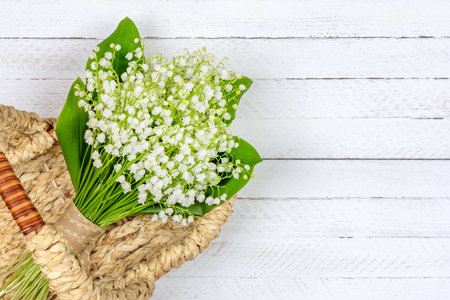 bouquet of Lily of the valley flowers in a basket on a white wooden background with a copy space close up top viewの写真素材